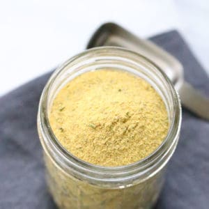 Overhead shot of vegan chicken seasoning in a small clear jar with teaspoon beside