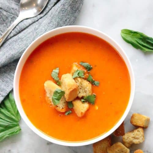 overhead shot of vegan tomato soup in a white bowl with garnish of croutons and chopped spinach