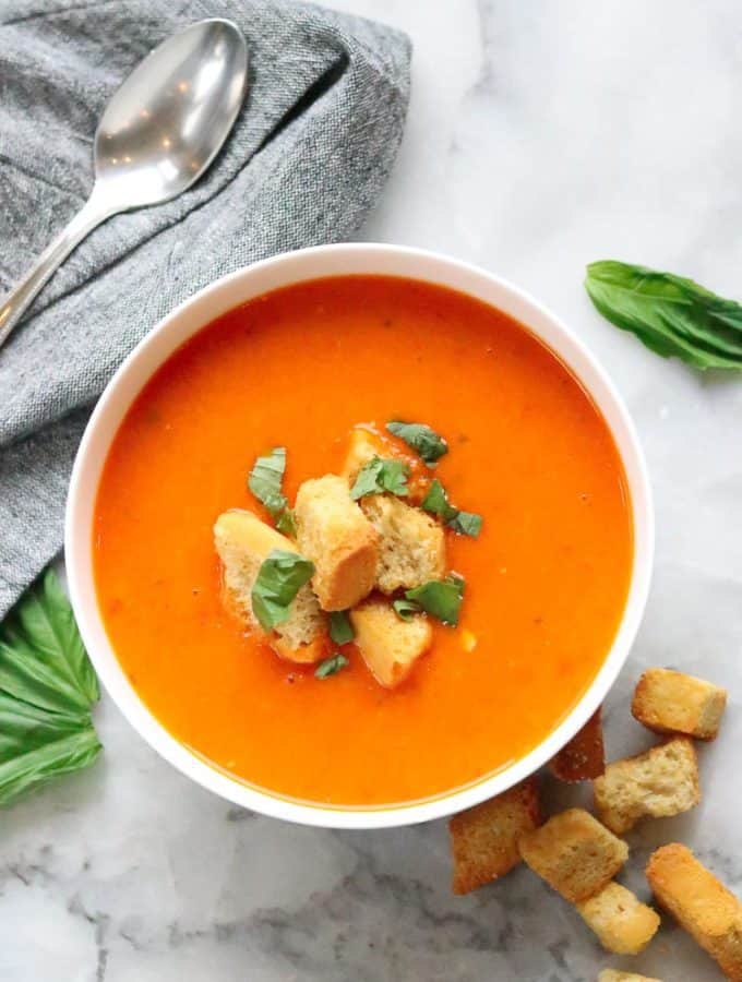 overhead shot of vegan tomato soup in a white bowl with garnish of croutons and chopped spinach