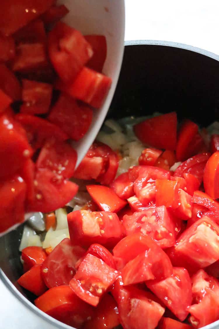 side shot of chopped fresh tomatoes being added to stock pot tomato soup mixture