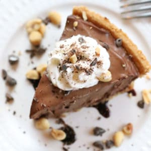 overhead shot of vegan peanut butter pie with whip cream, chopped peanuts and chocolate topping