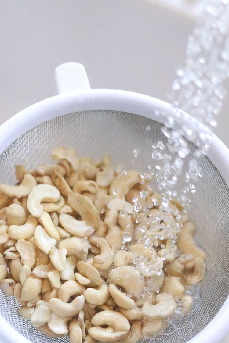 overhead shot of cashews in a colander being rinsed under running water
