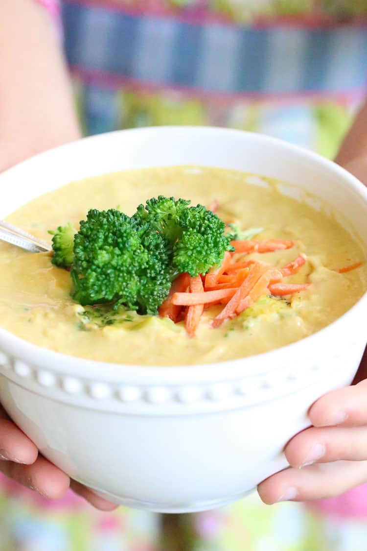 side view of vegan broccoli soup being held by two hands in a white bowl with apron in the background