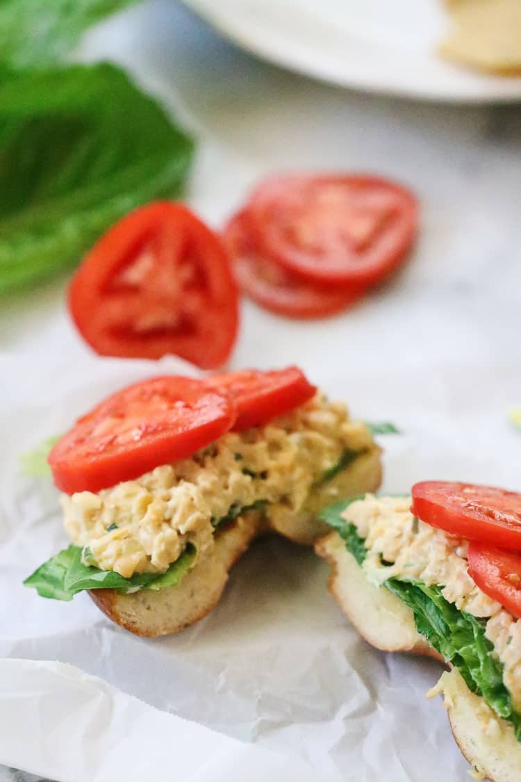 overhead side shot of vegan chickpea salad sandwiches with tomato slices on white parchment paper