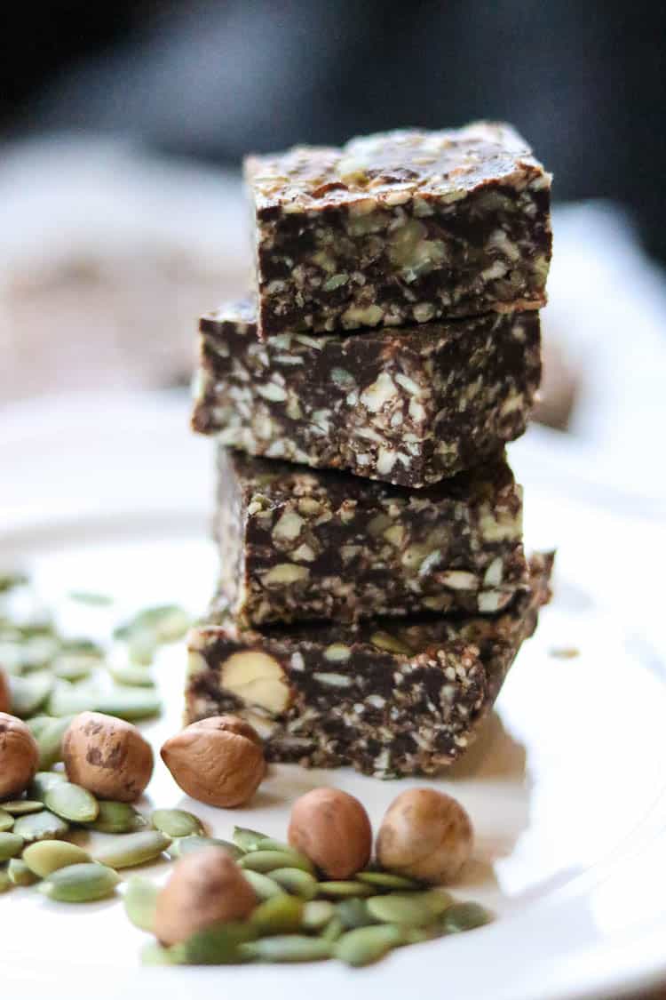 side view of stacked chocolate gingersnap bars with hazelnuts and pumpkin seeds in the foreground