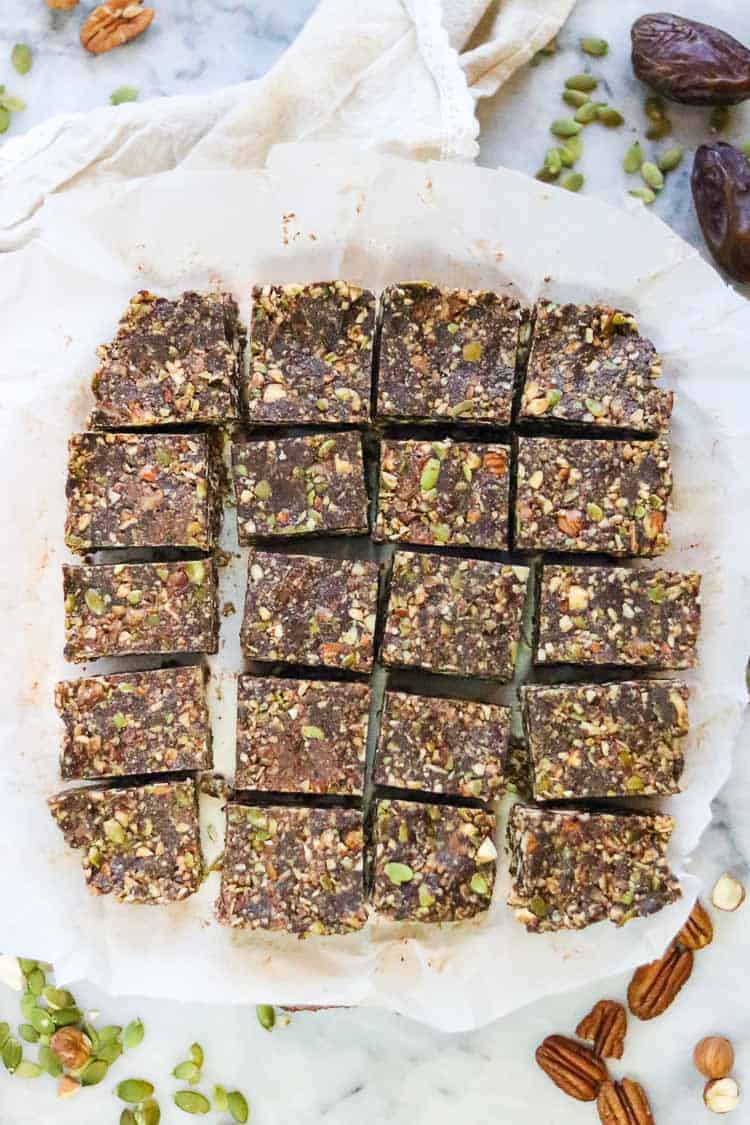 overhead shot of cut vegan chocolate gingersnap bars with nuts, dates, seeds, and napkin surrounding