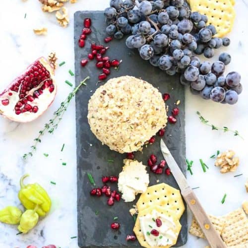 wide overhead shot of vegan cheese ball with crackers on black slate with pomegranates and grapes surrounding