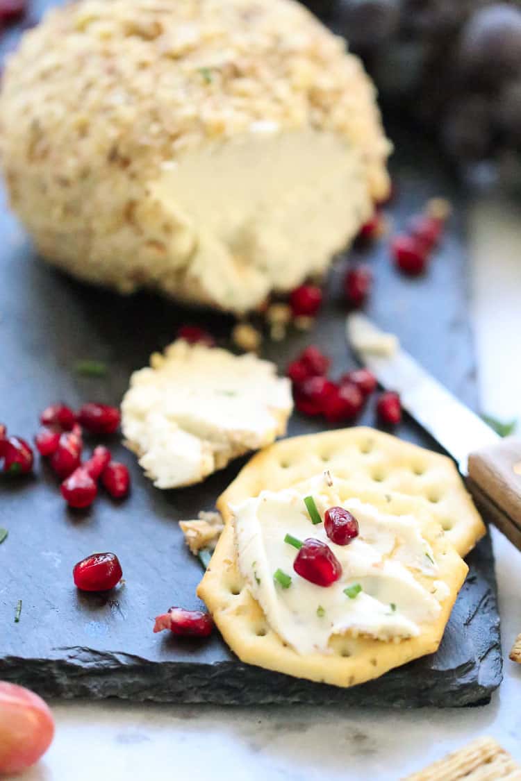 overhead side shot of vegan cashew cheese ball on slate platter with pomegranate seeds and crackers