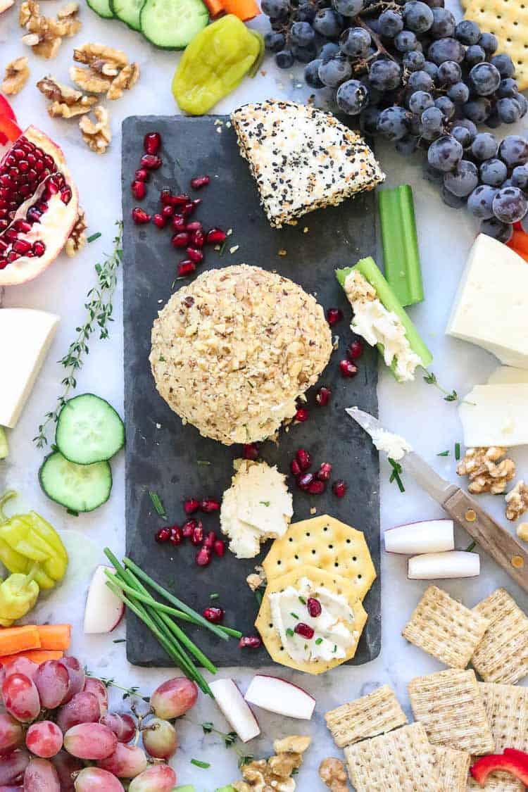 overhead shot of vegan cheese ball surrounded by fruit veggies and crackers on a marble cheese platter