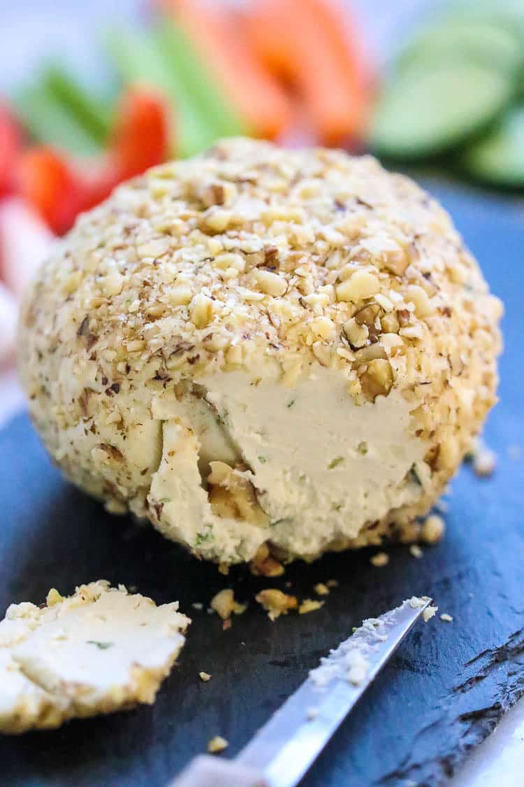 side closeup shot of vegan cheese ball sliced with knife beside