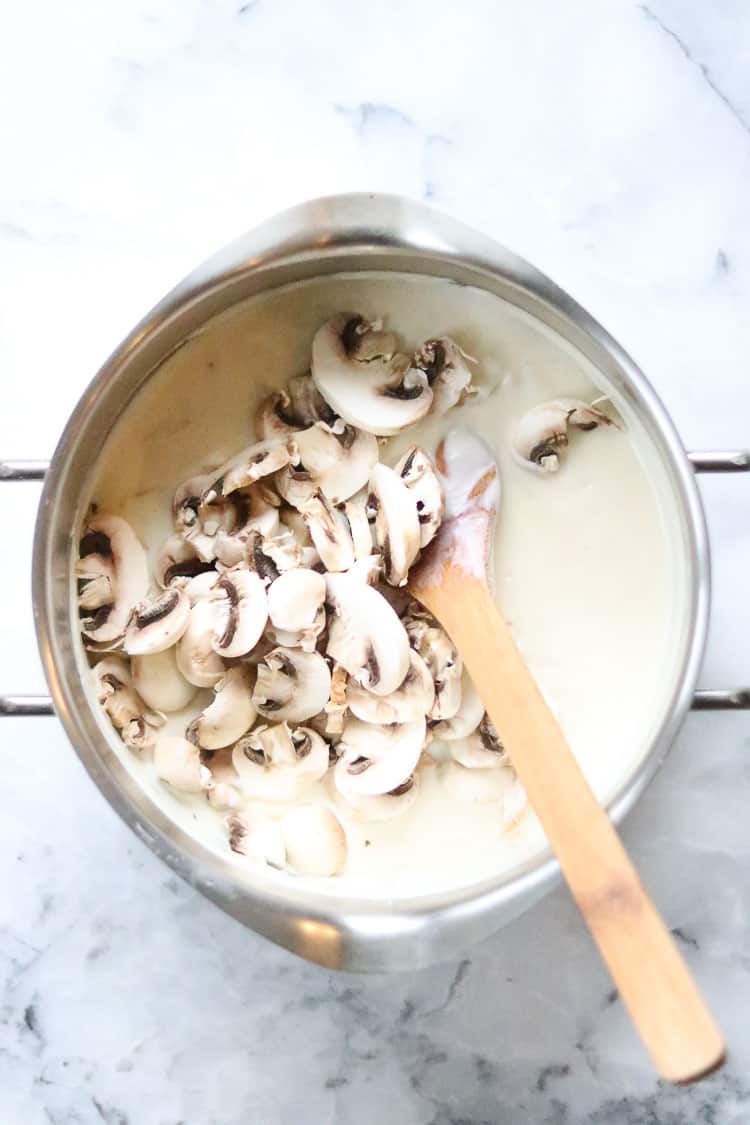 overhead shot of fresh mushrooms being added to white sauce for wild rice casserole in a silver pan