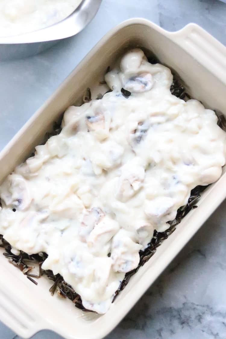 overhead shot of béchamel white sauce layered over wild rice in casserole dish