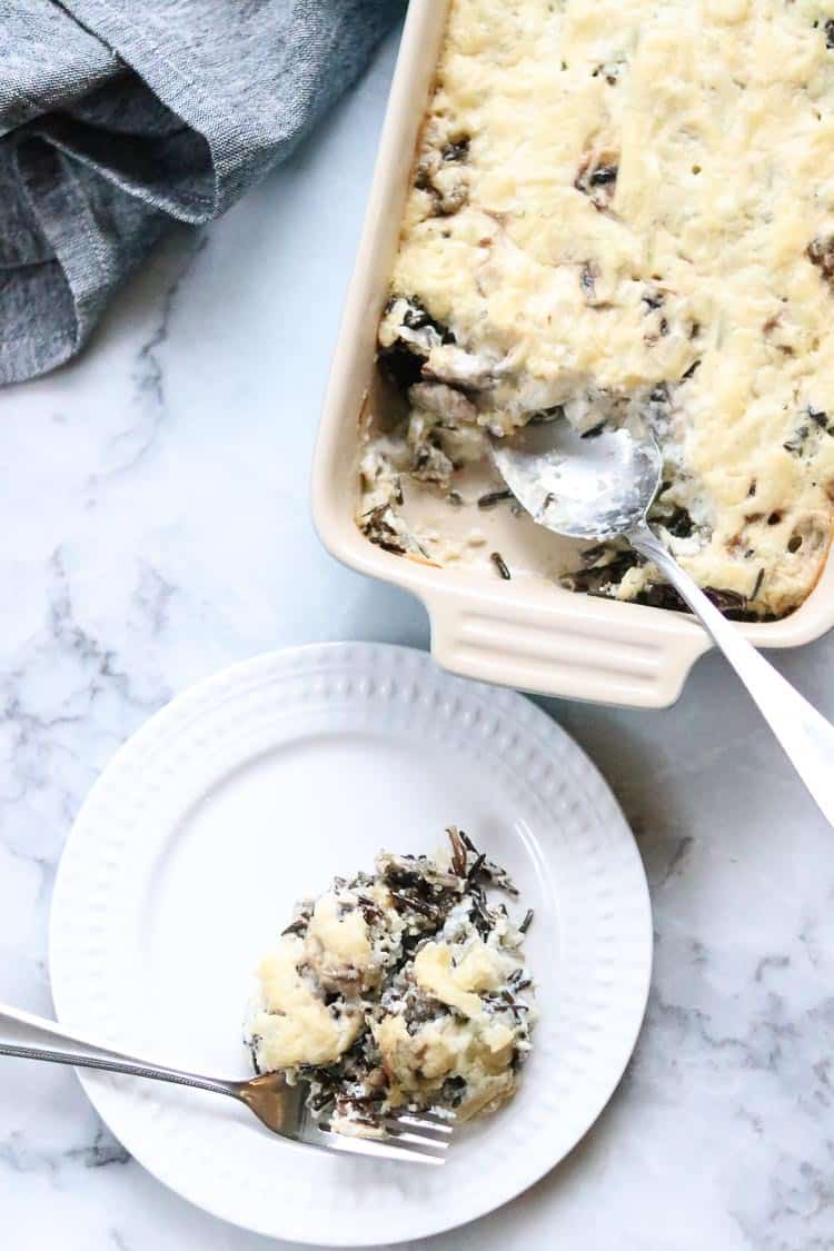 overhead shot of vegan wild rice casserole with a spoon and serving plate beside