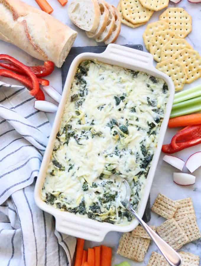overhead shot of vegan spinach artichoke dip surrounded by veggies, crackers and bread