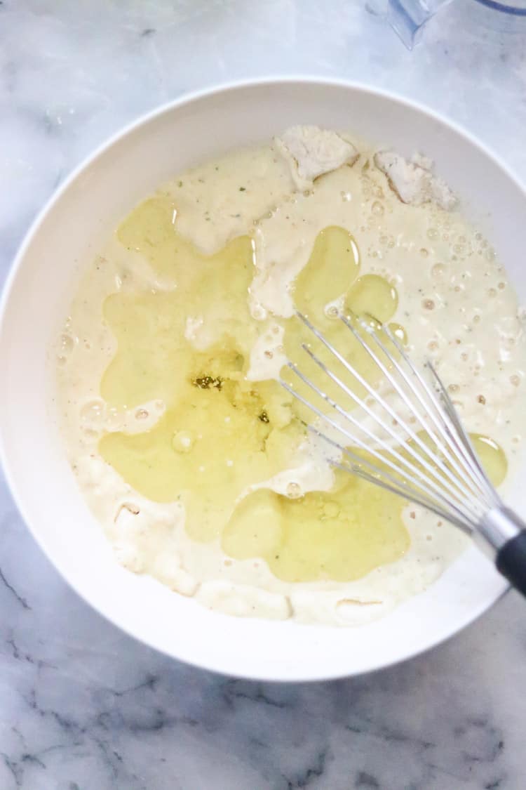 overhead shot of oil and vegetable broth being added to masa flour in white bowl for vegan tamale dough