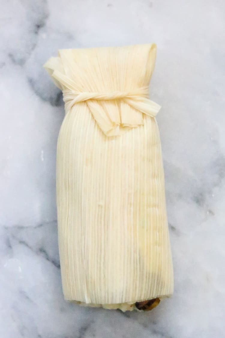 overhead shot of tied and wrapped vegan tamale on white marble background