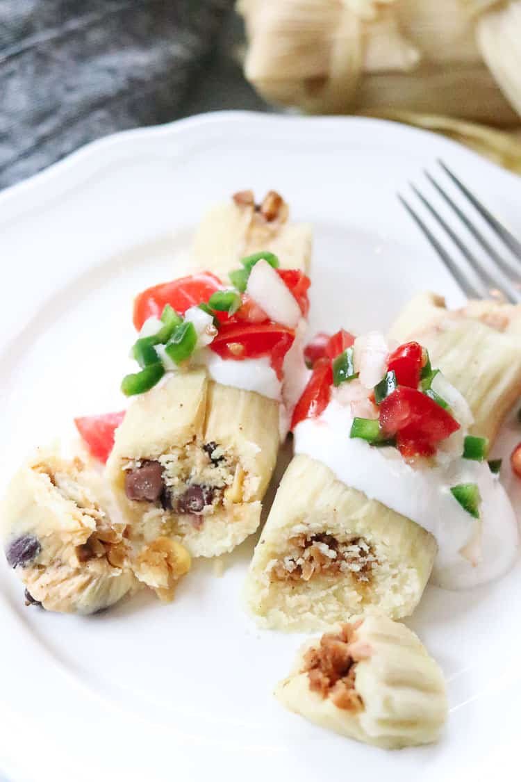 overhead closeup side shot of vegan tamales being served on white plate with sour cream and pico de gallo
