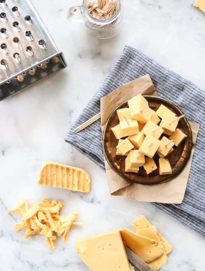 overhead shot of vegan cheddar cheese on white marble in shredded, cubed, sliced and block form