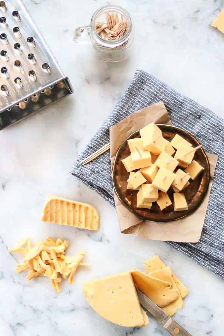 overhead shot of vegan cheddar cheese sliced, cubed and grated agains a marble background