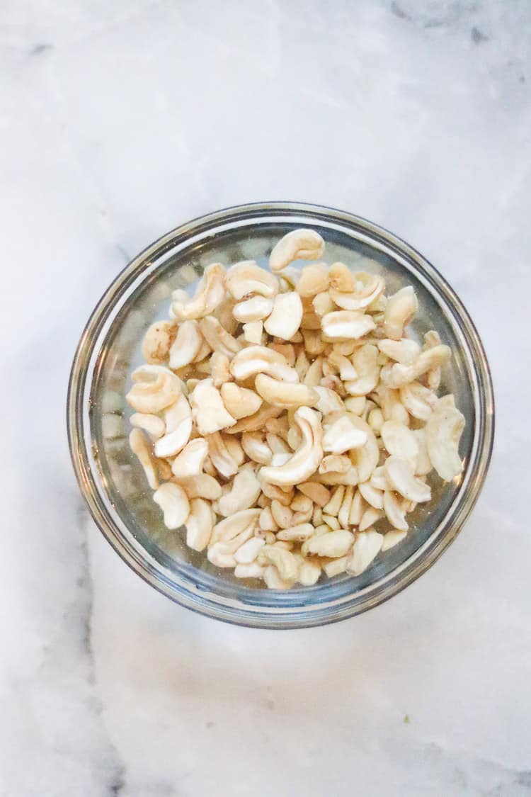overhead shot of cashews soaking in clear bowl for vegan cheddar cheese making