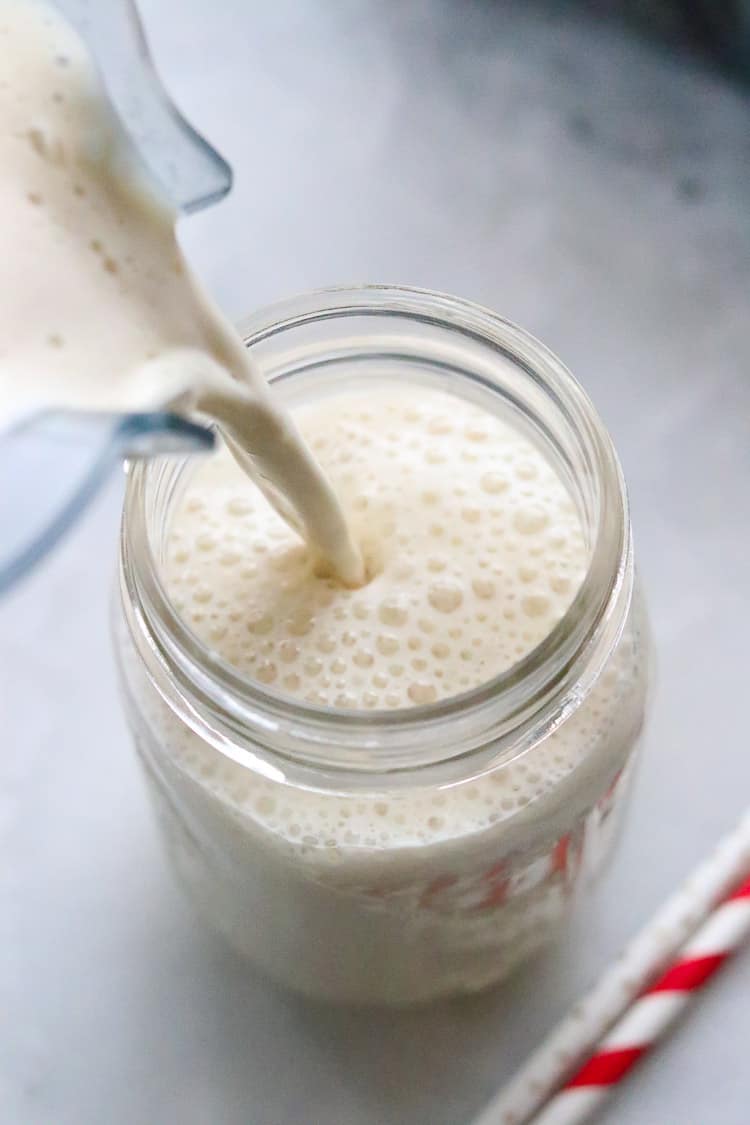overhead shot of dairy free eggnog being poured from blender into glass jar with straws beside