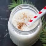 overhead shot of vegan eggnog in a small mason jar with two straws and greenery in background
