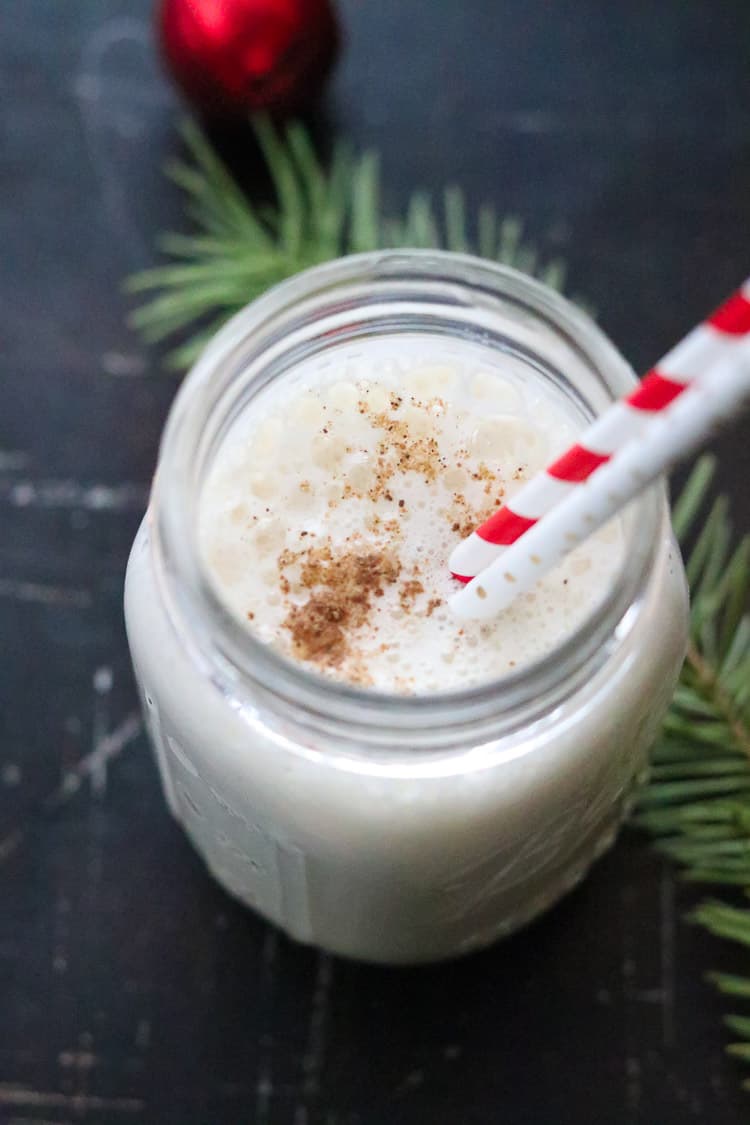 overhead shot of vegan eggnog in a small mason jar with pine bough and red bell nearby