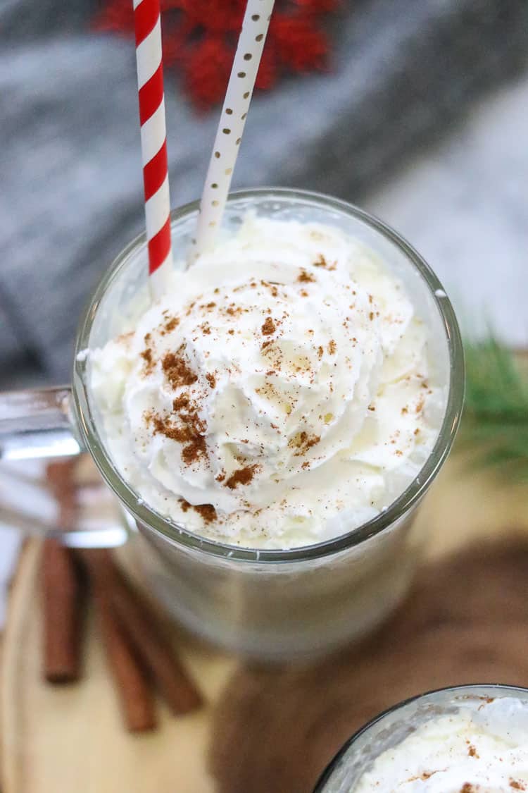 overhead shot of vegan eggnog in a clear glass with handle with two straws in it