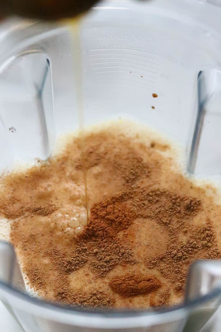overhead side shot of maple syrup being poured into blender contents for vegan eggnog