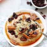 side overhead shot of bowl of buckwheat porridge garnished with cranberries, pecans, and hempseed on a diamond napkin