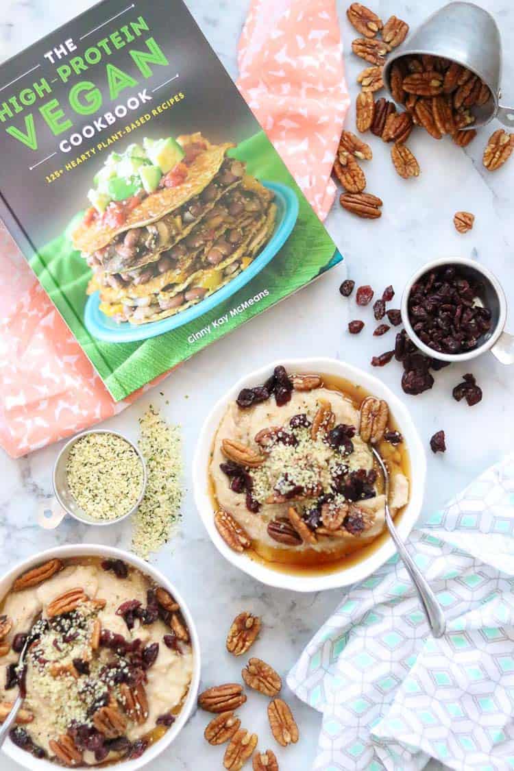 overhead shot of two bowls of buckwheat porridge with garnishes beside as well as the high protein vegan cookbook in the background