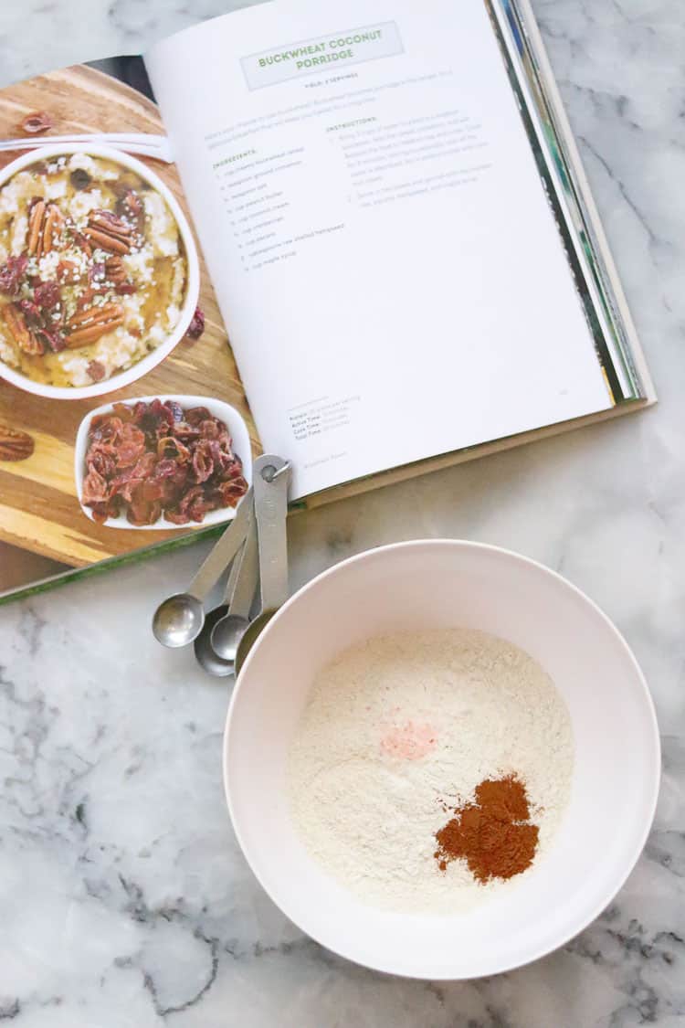 overhead shot of open cookbook beside a white mixing bowl with buckwheat flour, salt, and cinnamon measured into it