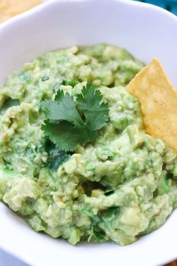 overhead closeup shot of guacamole in a white bowl with a garnish of fresh cilantro