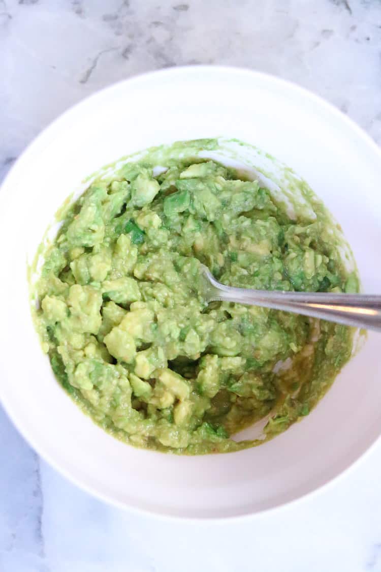 overhead shot of mixed and mashed guacamole in a white mixing bowl with a silver fork in it