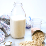 side shot of oat milk jug surrounded by oats, agave, vanilla with text overlay for pinterest graphic