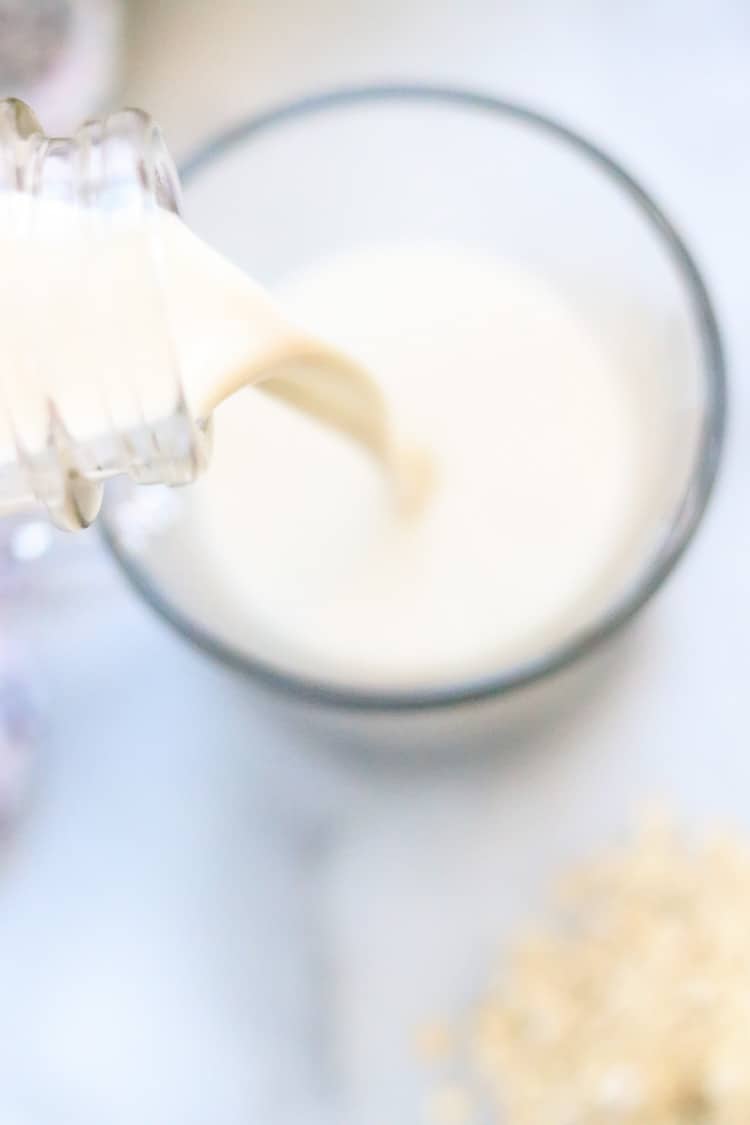 overhead shot of oat milk being poured into clear glass cup