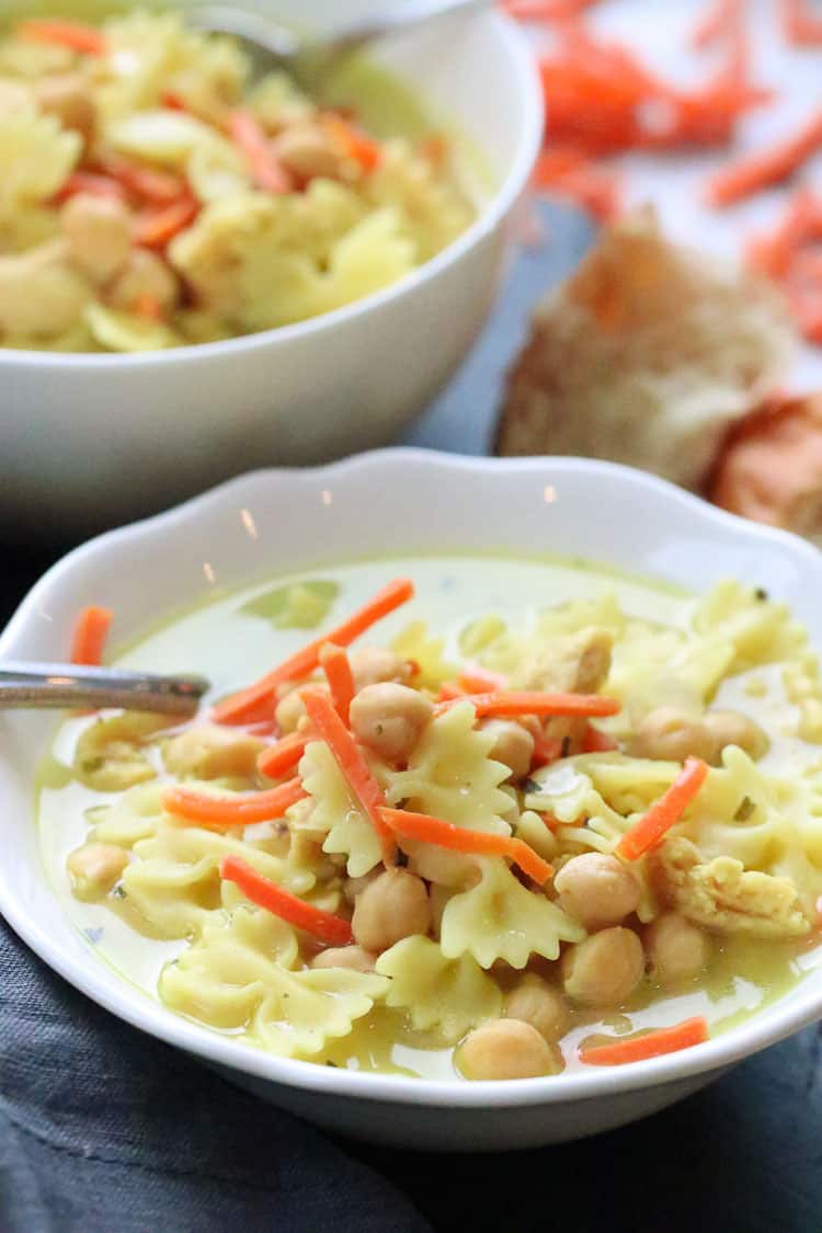 side overhead closeup shot of vegan chicken noodle soup in white bowl with shredded carrots on top and behind bowl