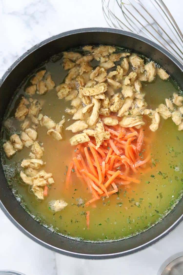 overhead closeup shot of stock pot filled with ingredients for vegan chicken noodle soup