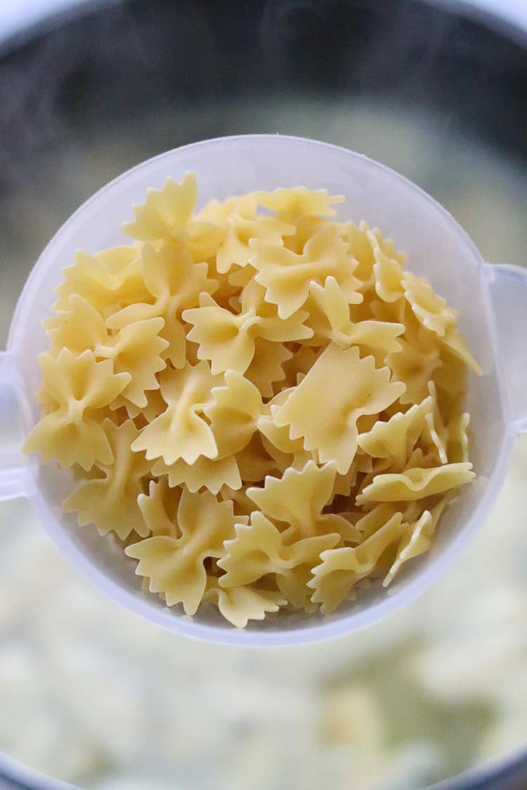 overhead closeup shot of pasta bowties in a measuring cup held over steaming stock pot