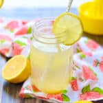 side shot of lemon water in a jar with cut lemon on jar rim and white straw in it