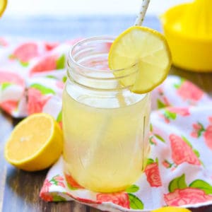 side shot of lemon water in a jar with cut lemon on jar rim and white straw in it