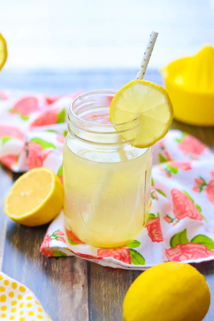 side overhead shot of mason jar glass of lemon water with halved lemon beside on wooden surface with lemon squeezer in background