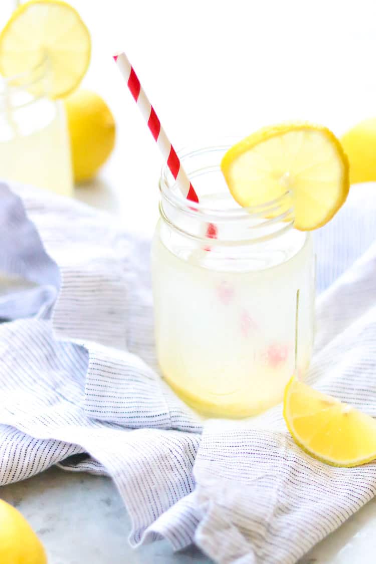 side overhead shot of single glass of lemon water with lemon wedge beside on blue striped napkin and second glass in background