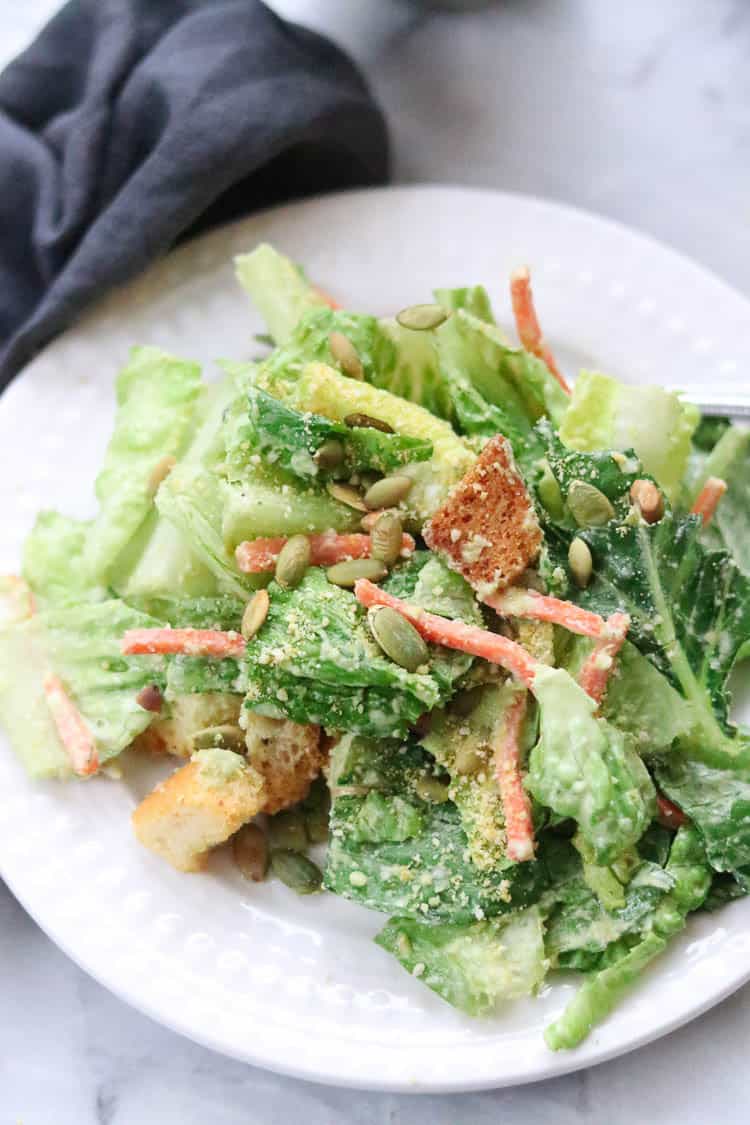 side overhead shot of vegan caesar salad dished up on a white plate with pumpkin seed and crouton garnish