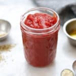 side overhead view of pizza sauce in a small clear jar with ingredients in measuring cups nearby