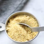 overhead picture of vegan parmesan cheese in a silver measuring cup with tablespoon in it