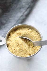 overhead picture of vegan parmesan cheese in a silver measuring cup with tablespoon in it