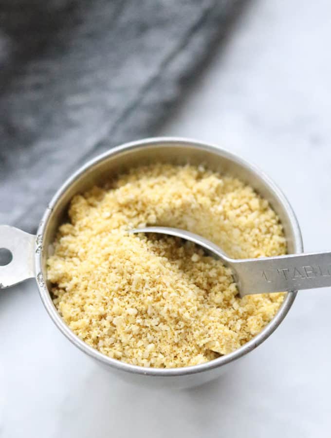 overhead picture of vegan parmesan cheese in a silver measuring cup with tablespoon in it