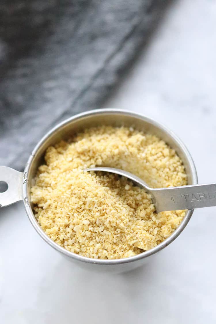 side overhead shot of grated vegan parmesan cheese in a silver measuring cup