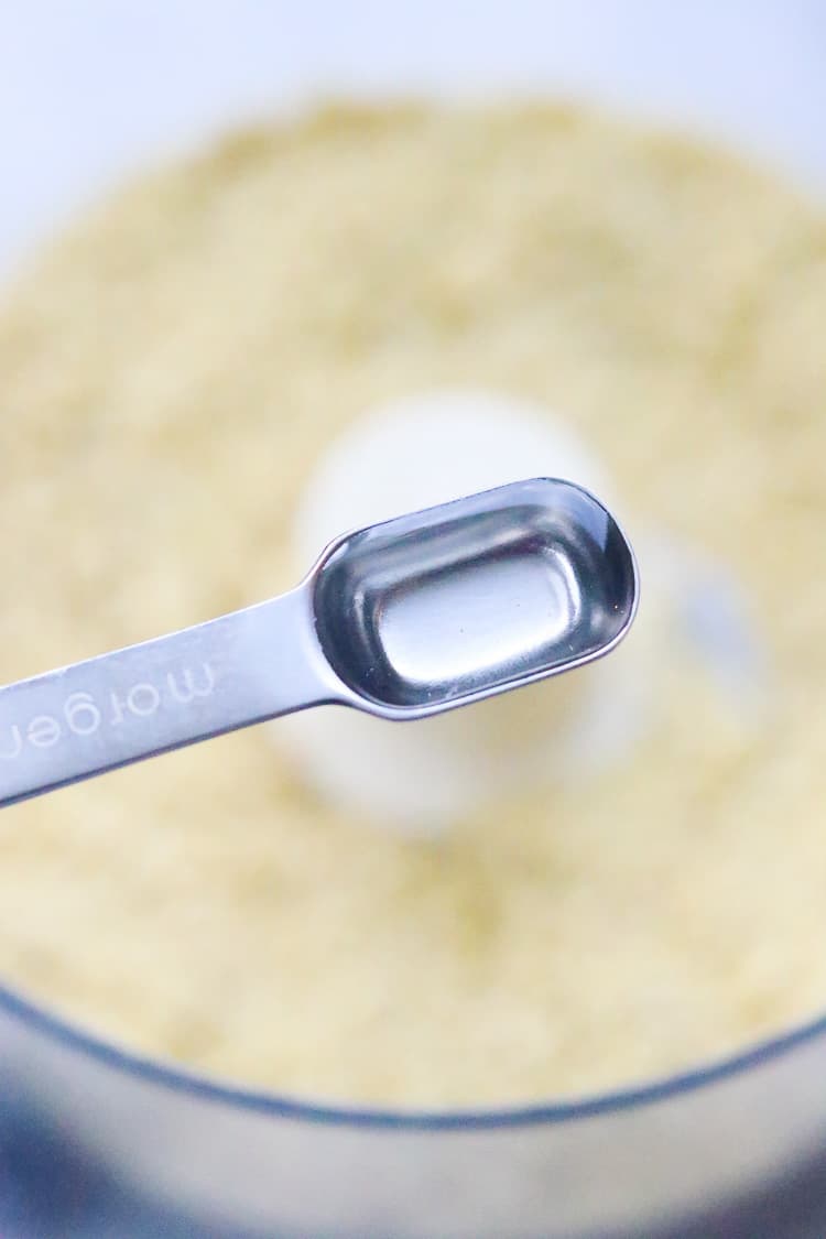 overhead closeup shot of white vinegar in measuring spoon to be added to grated vegan parmesan cheese mixture